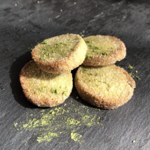 Quatre biscuits ronds saupoudrés de thé matcha vert sont déposés sur une ardoise
