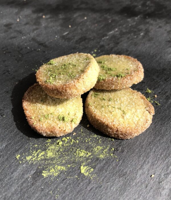 Quatre biscuits ronds saupoudrés de thé matcha vert sont déposés sur une ardoise