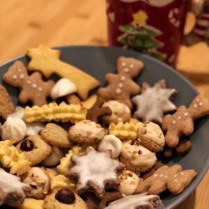 assiete creuse avec pleins de biscuits de noel en forme d etoile d oursons ou de sapin. une tasse sous le theme noel a cote