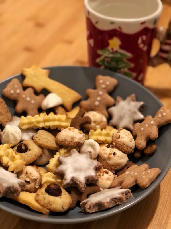 assiete creuse avec pleins de biscuits de noel en forme d etoile d oursons ou de sapin. une tasse sous le theme noel a cote