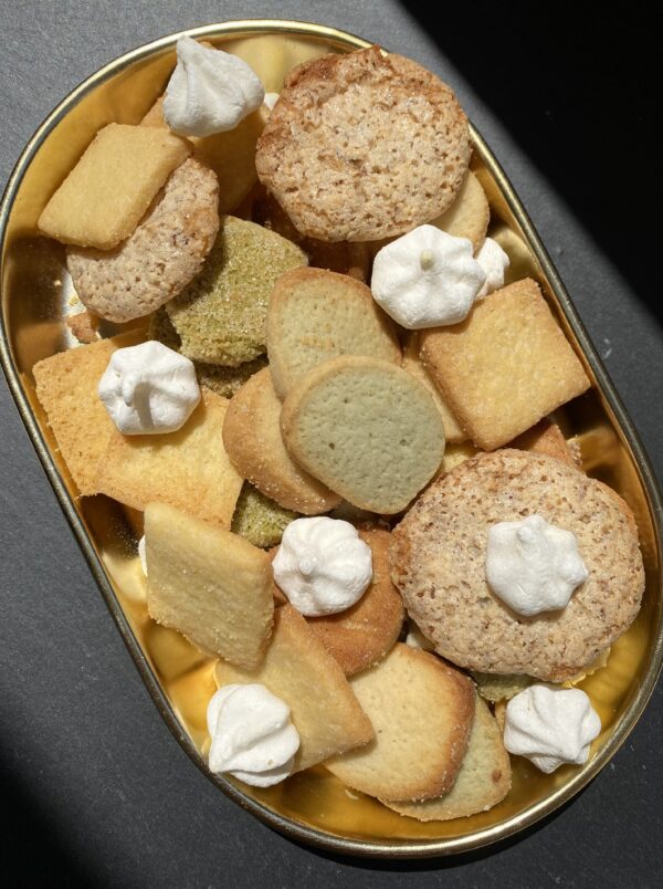 coupelle dorée sur fond noir avec biscuits ronds et carrés et petites meringues